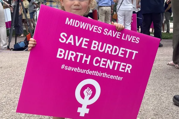 Baby holding pink Save Burdett Birth Center sign