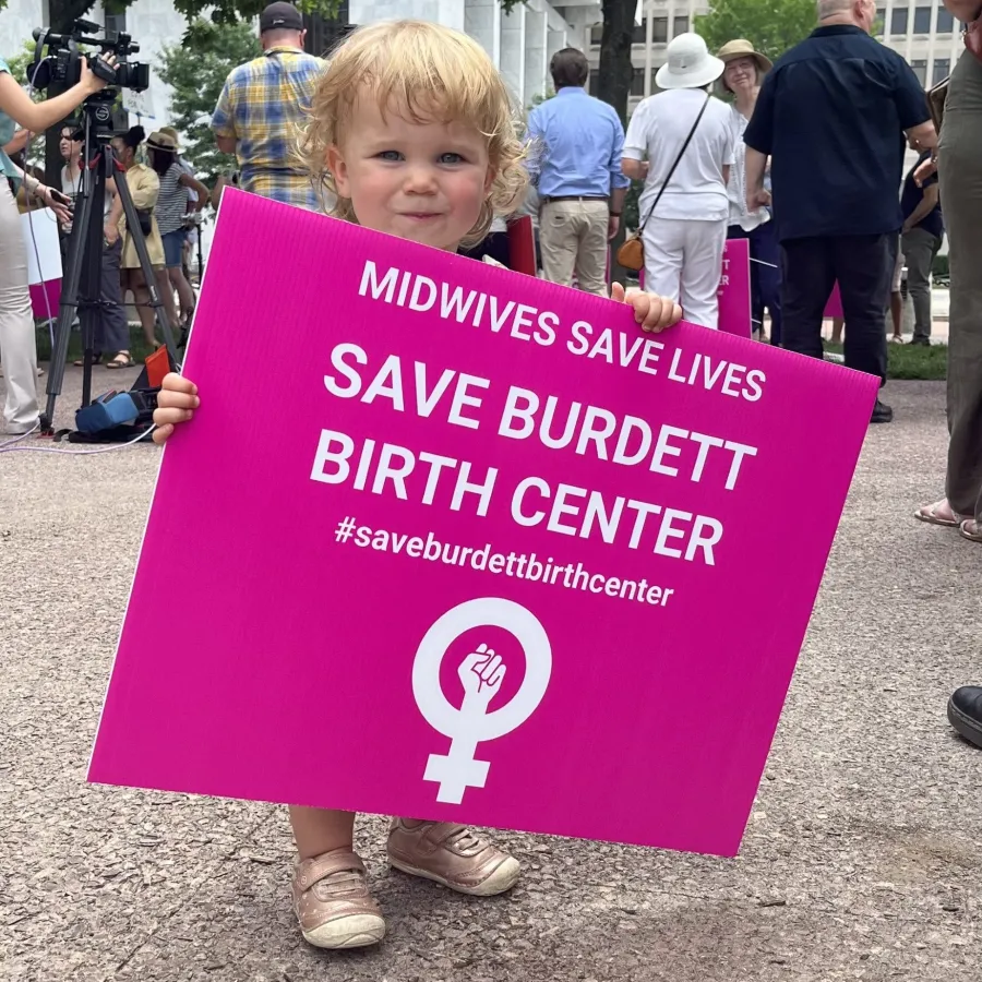 Baby holding pink Save Burdett Birth Center sign